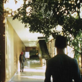 Filmstill einer Person in der Rückenansicht in einem Flur. 