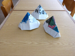 Gefaltete Papierhüte, die mit Aquarellfarbe bemalt sind.