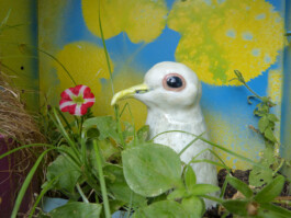 Weiße Taube aus Ton zwischen Pflanzen.