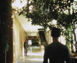 Filmstill von einer Person in Rückenansicht in einem Flur.