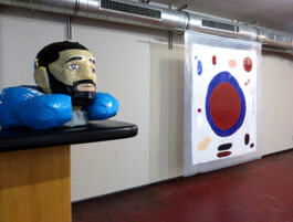 Büste aus Pappmache und Tesafilm auf einem tresen und ein abstraktes Bild im Hintergrund.