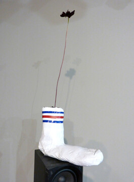 Objekt aus Pappmache und Tesafilm das aussieht wie eine Tennissocke mit einer Blume. 