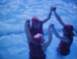Filmstill von drei Personen in einem Schwimmbecken, die Wasserballett machen.