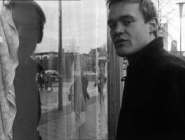 Filmstill von einem Mann, der sich in einem Schaufenster spiegelt.
