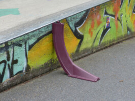 Ein lilafarbenes gebogenes Plastikteil das neben einem Hindernis des Skateparks steht.