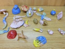 Verschiedene kleine farbige Skulpturen aus Ton, beispielsweise ein Schmetterlin, ein Vogel, ein Pilz, eine Schlange und ein Schwein.