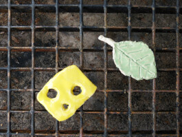 Eine Scheibe Käse aus Ton und ein Blatt aus Ton liegen auf einem Grill.