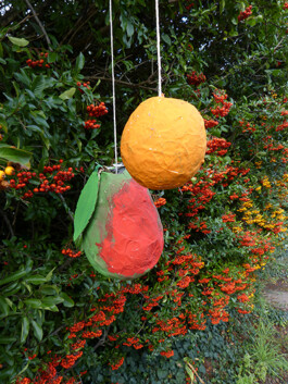 Eine Birne und eine Orange aus Pappmaché hängen im Garten.