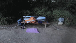 Filmstill von einer Parkbank, die Aufnahme stammt von einer obdachlosen Person.