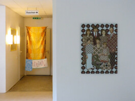 Ausstellungsraum mit einem Kunstwerk das aus Handtüchern hergestellt wurde und einem Gemälde einer Familie.